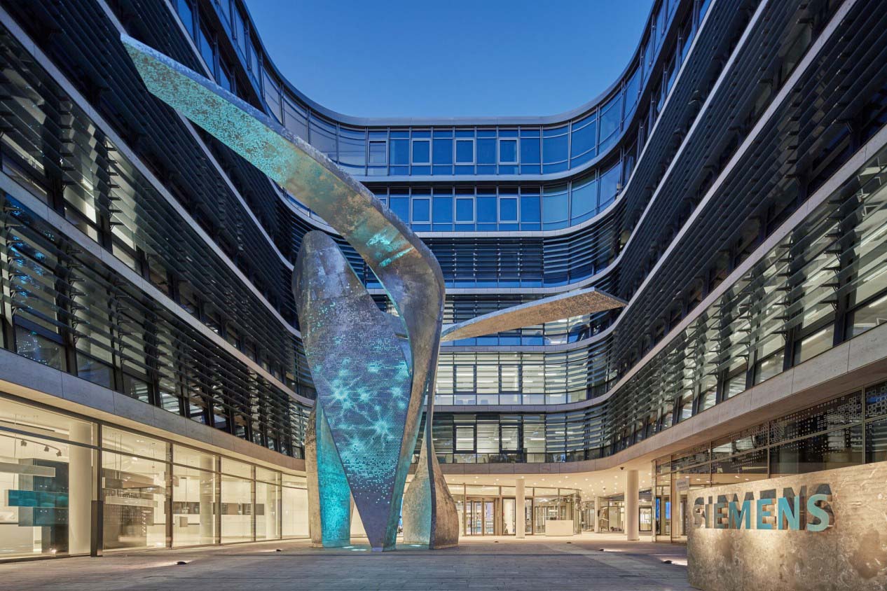 Die beleuchtete Skulptur namens Siemens Wings, bestehend aus drei in die Höhe ragenden und gebogenen Säulen, in der Mitte von Bürogebäuden