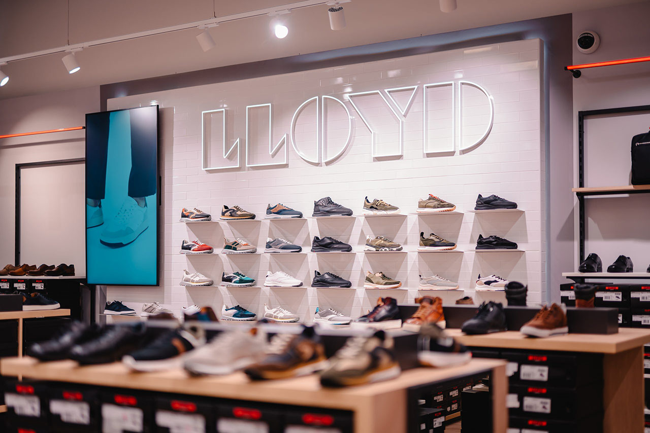 Sneakers, die an der Wand im LLOYD-Store ausgestellt sind, daneben ein Screen im Hochformat auf dem Sneakers zu sehen sind