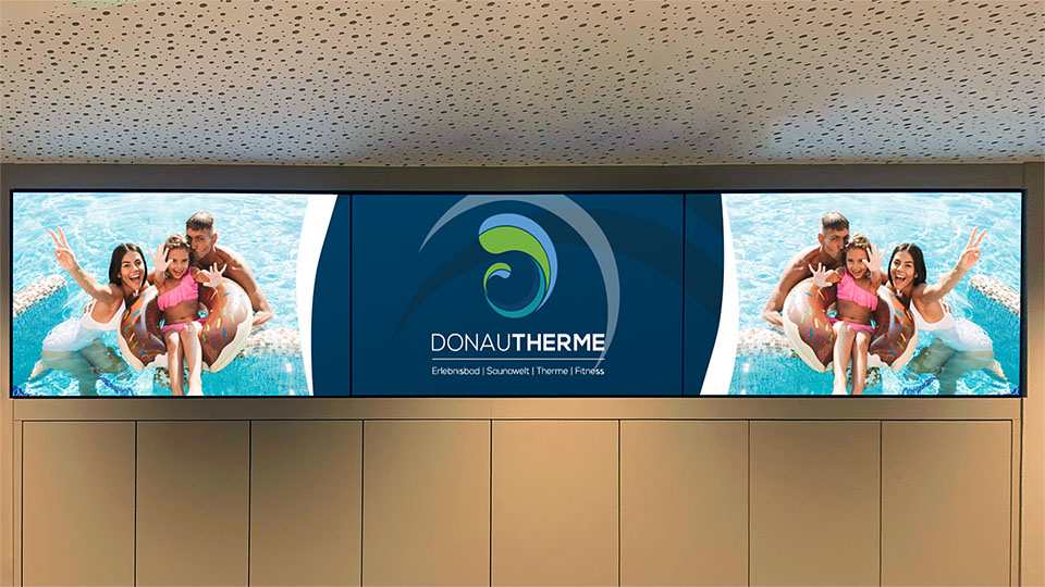 Drei Screens nebeneinander im Eingangsbereich der Donautherme mit Wasser-Content und Donautherme-Logo
